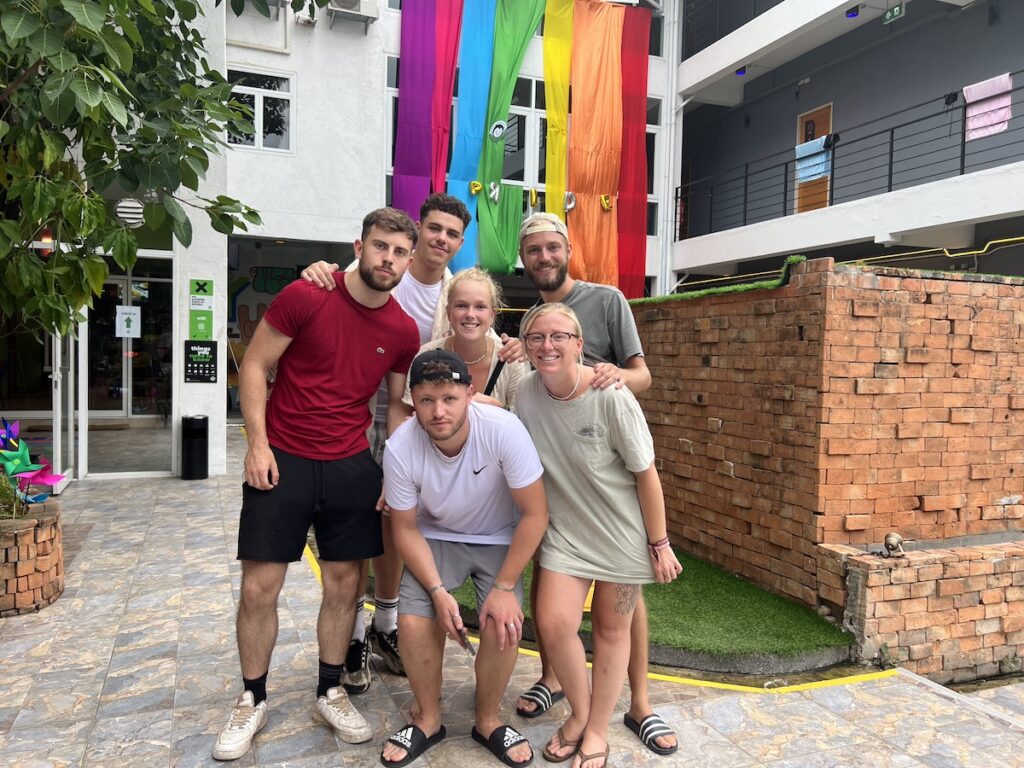 A group of people posing in front of a building with a rainbow banner during their budget-friendly trip to Thailand.