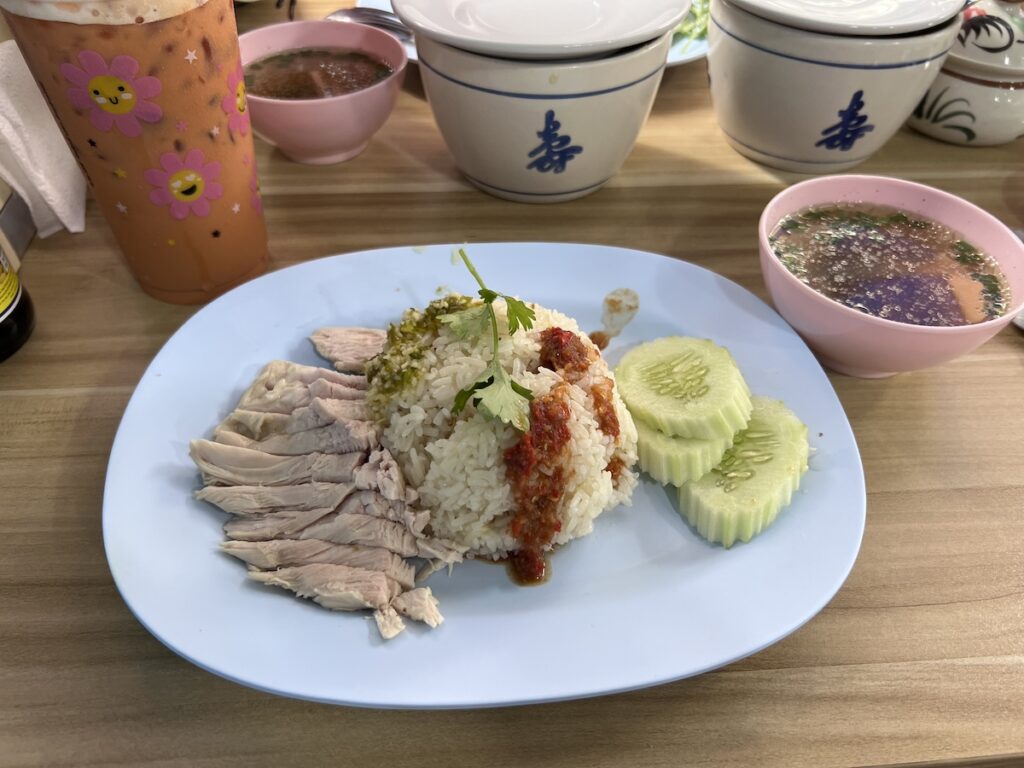 A plate of rice, chicken and cucumbers on a table in Thailand.