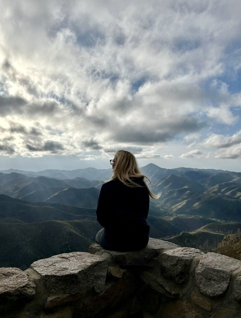 Solo Camping As A Woman: My Safety Tips & Advice When Camping Alone! 1 A solo camping woman sits on a rock overlooking the mountains.