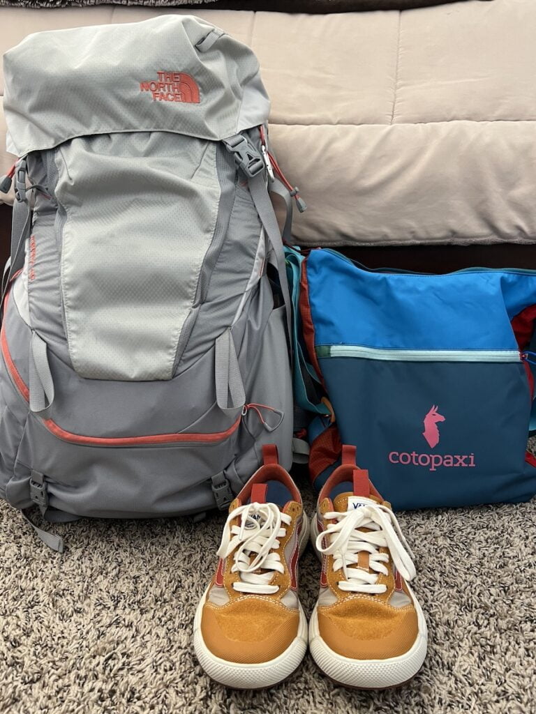 The north face backpack and shoes on a bed, perfect for a budget-friendly trip to Thailand.