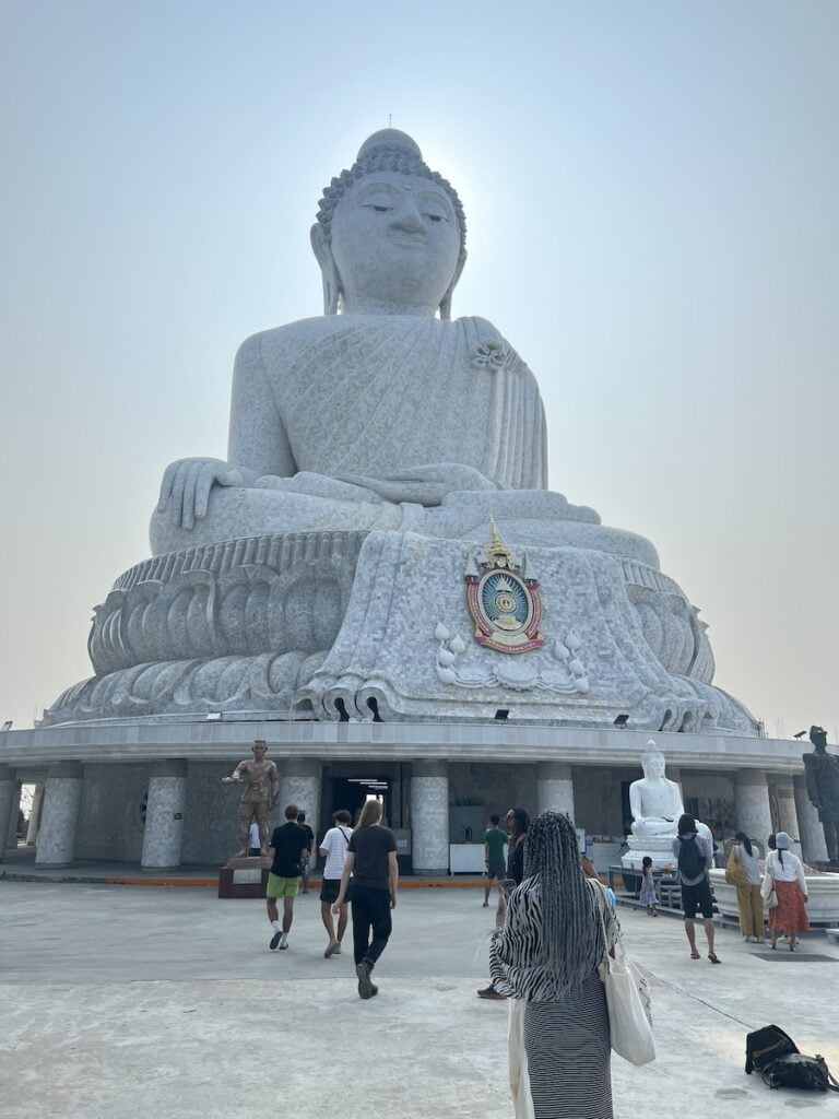 A group of people standing in front of a large white Buddha statue in Thailand, capturing the beauty and serenity while on a budget.