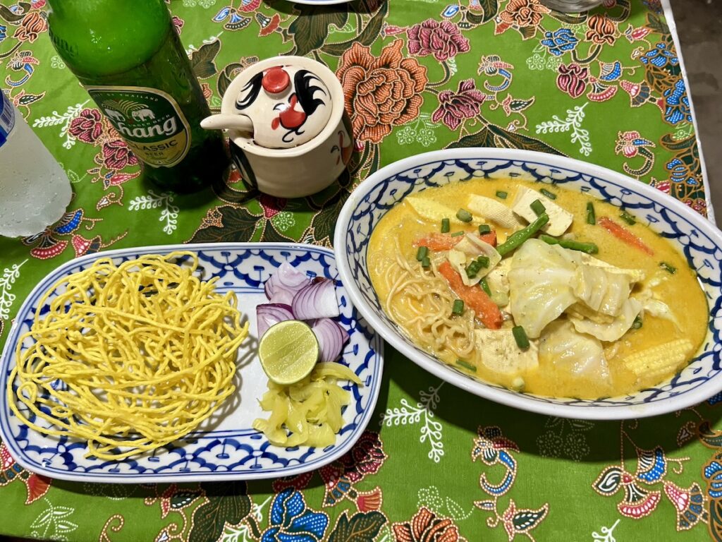 Two bowls of noodles from Thailand on a budget and a bottle of beer on a table.